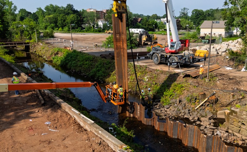 Workers assist with the installation of steel sheet piling.