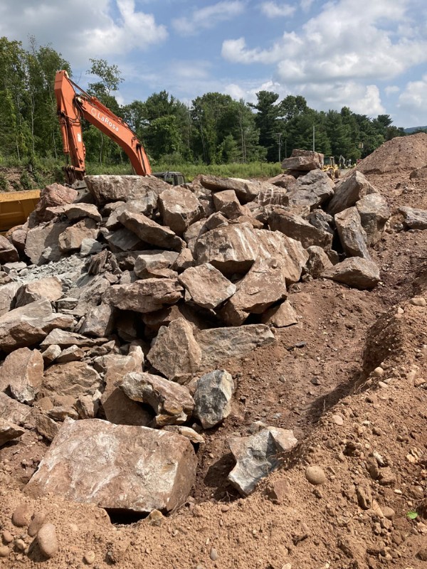 An excavator works to remove large rocks and grade the construction site.