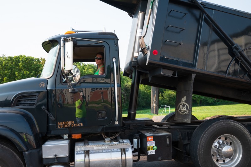 A worker shown in the driver’s seat of a dump truck while the bed is raised.