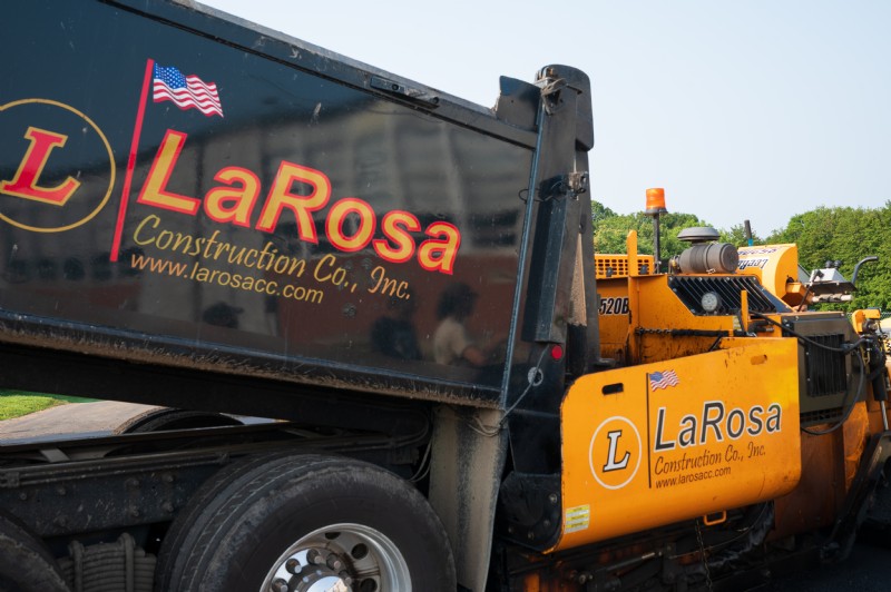 A dump truck and an asphalt paver in use, both with the LaRosa Construction logo on their sides.