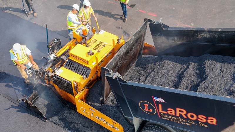 A dump truck with the LaRosa Construction logo on it being used to transfer asphalt mix into the paver’s hopper.