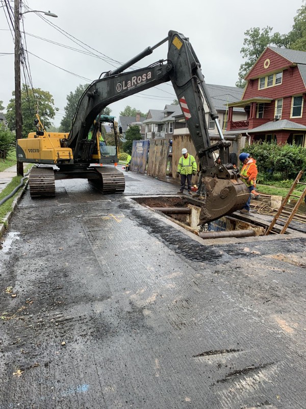 An excavator with the LaRosa logo excavates a segment of a residential street.