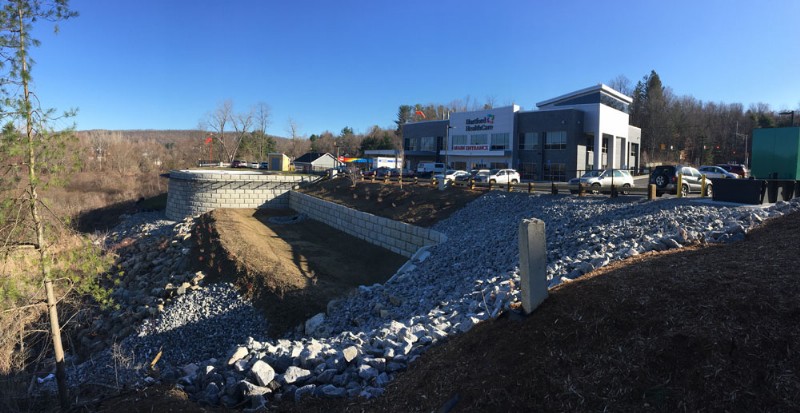 The medical building development site with a large retaining wall, rock and gravel fill, and grading on a sloped area.