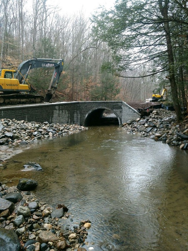 Heavy machinery being operated on both sides of the bridge, with Walker Brook in the foreground.
