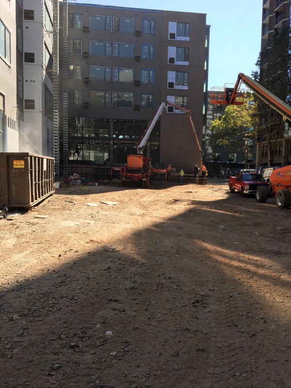 The cleanly excavated, backfilled, and graded construction site, with cranes working on new buildings in the background.