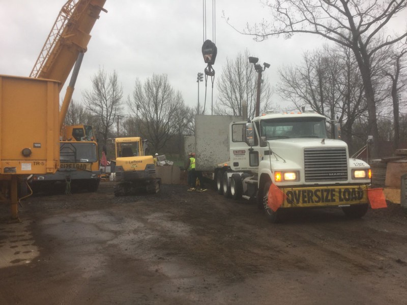 A crane prepares to lift a large concrete block off a flatbed truck.