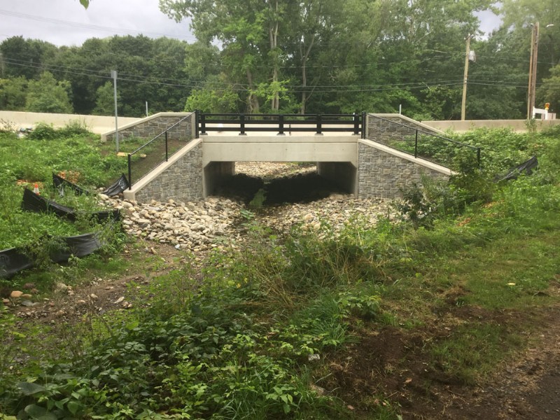 The completed bridge over Wintergreen Brook, seen with gravel and rock along both banks. 