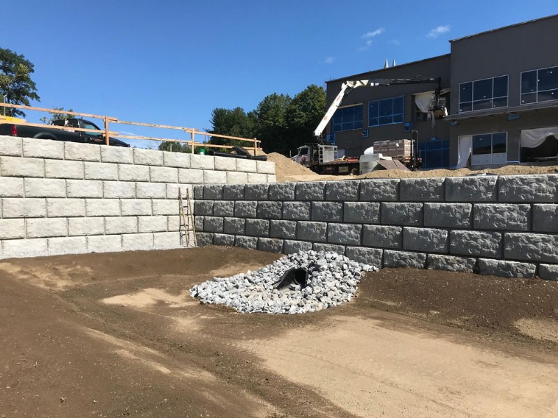 Heavy-duty precast concrete blocks installed to create a large retaining wall, with a drainage area visible at its base.
