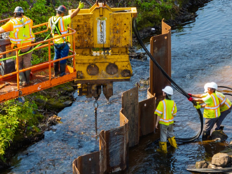 Workers positioned on a crane and in Harbor Brook while working to replace the bridge.