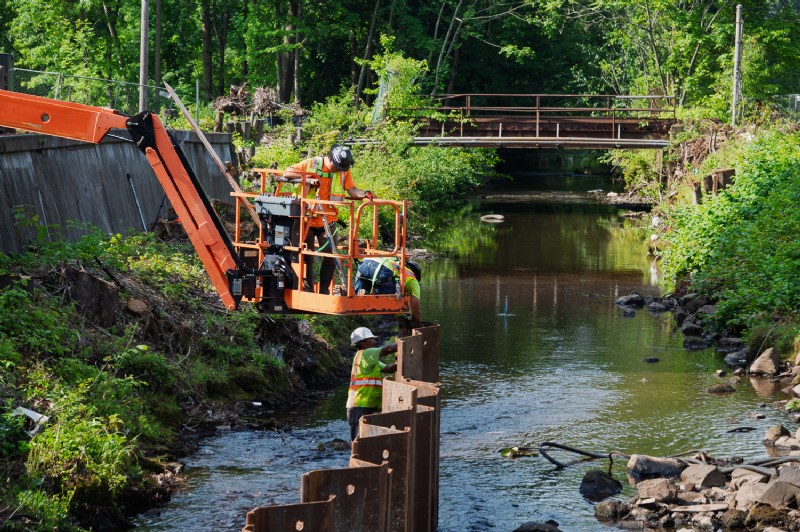Close-up of workers installing steel sheet piles in Harbor Brook as part of the bridge replacement project.