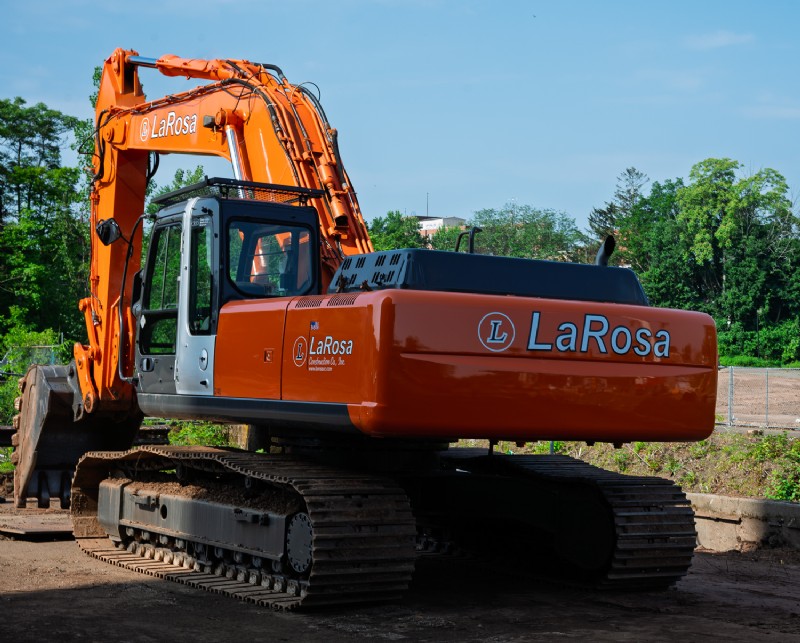 A heavy-duty excavator featuring the with the LaRosa Construction logo clears and grades land around the construction site.